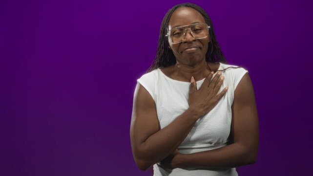Young woman in white sleeveless top with hand on chest, subtle smile and closed eyes, gesture of relief in studio; gratitude.
