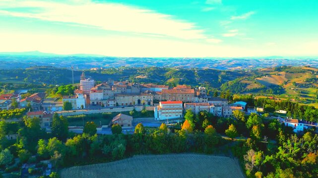 Beautiful aerial push-in shot from Monte Rinaldo, approaching the town centre and its manifold buildings, arches, trees, streets, with a vision of perfect Marche hills surrounding it, under veiled sky