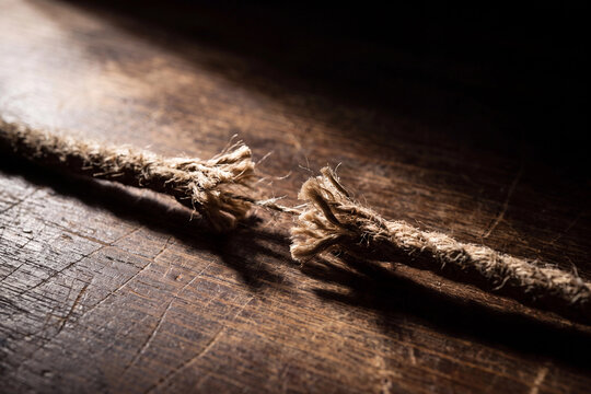 Frayed rope breaking apart on a dark wooden surface for reaching breaking point stress limit financial strain and business failure risk concept