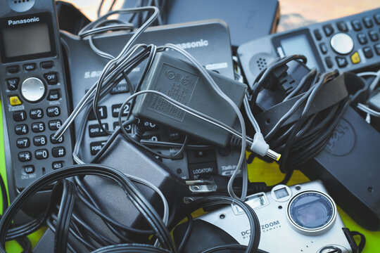 Pile of outdated and discarded consumer electronics, including old landline phones, chargers, and a digital camera. Editorial Use Only.