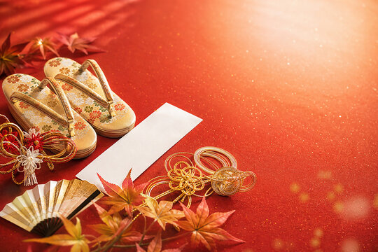 Japanese traditional gold zori sandals, mizuhiki knots, folding fan and autumn maple leaves on a red background with blank white card for text, 金の草履と水引 扇子と紅葉を配した赤い和風背景 文字入れ用の白い短冊付き お祝いイメージ