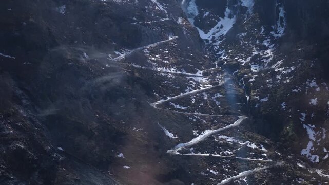 Winding mountain road and snowy slopes with waterfalls in Norways Aurlandsfjord valley