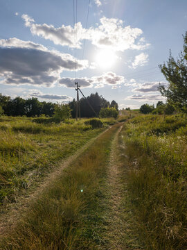 Country Dirt Track Facing Bright Sun Shining Through Sky Clouds
