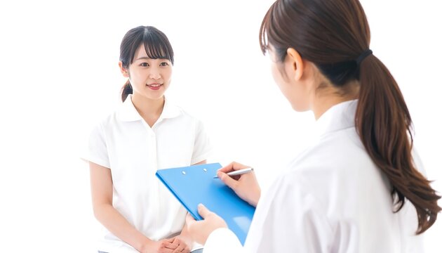 A young woman smiles as she answers questions for a health professional taking notes on a clipboard. The background is white