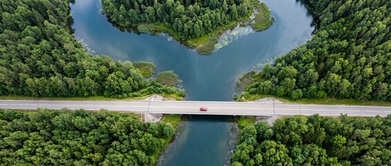 Obraz premium Aerial view of a road bridge over a river flowing through a dense green forest