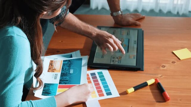 Top view of manager writing idea on sticky notes and explain idea about web design. Professional marketing team or programmer brainstorming idea while looking at tablet with color palette. Symposium.