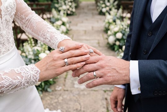Closeup of a bride and groom holding hands and showing off their wedding rings during a ceremony