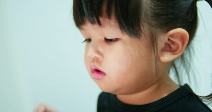 Little girl sits in the living room focused on her tablet screen. She interacts with an educational app, depicting modern parenting, smart device usage, and indoor childhood leisure.