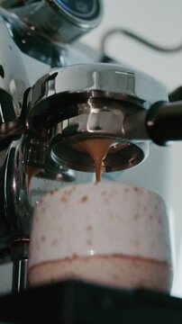 4K Pouring coffee stream from professional machine in cup. Barista man making double espresso, using filter holder. Flowing fresh ground coffee. Drinking roasted black coffee in the morning.	
