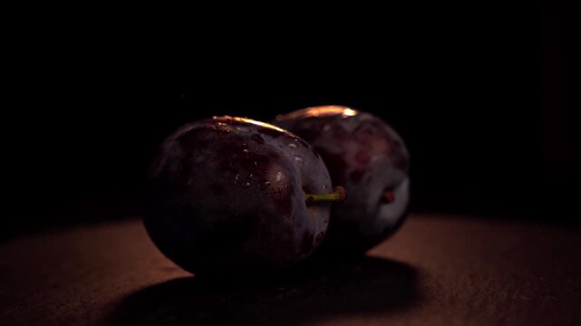 Two fresh juicy plums resting on dark slate surface illuminated by