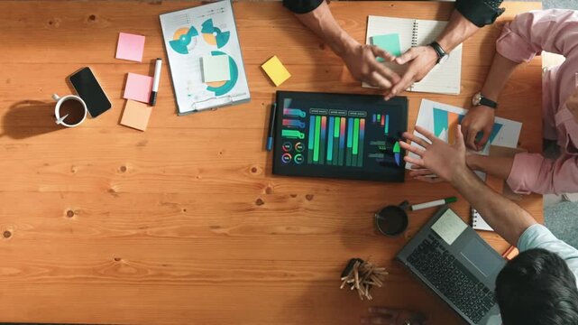 Top view of skilled project manager talking about financial graph to investors while sitting at meeting table with data analysis document. Diverse team discussing and brainstorming idea. Convocation.