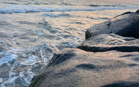 Ocean waves crashing against coastal rocks. Sea water splashing on stone shore at sunset.