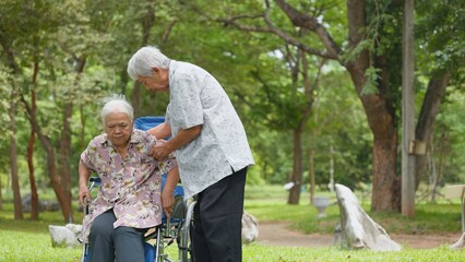 Fototapeta premium Happy Asian senior couple enjoying time together in park with wheelchair assistance. Elderly healthcare, supportive loving relationship, and golden years retirement lifestyle.