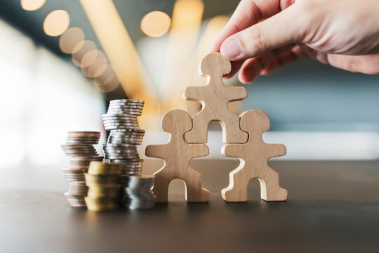 Hand building wooden human structure with stacked coins financial investment teamwork organizational growth family insurance planning savings stability concept.