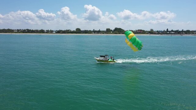 Aerial drone view of a parasailing boat launching a colorful green and yellow parachute over the turquoise waters of Captiva Beach, Florida.