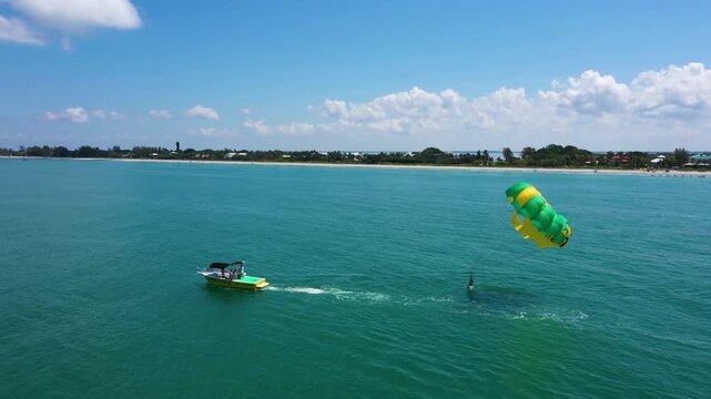 Drone footage of a parasailing adventure off Captiva Beach, Florida, capturing the vibrant parachute, speeding boat, and shimmering emerald sea.