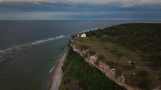A lighthouse cottage stands on high sea cliffs on Gotland, Sweden, beneath fading dusk light and a wide coastal horizon.