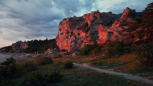Limestone cliffs tower above a rocky shoreline during golden hour in Sweden, with warm sunlight highlighting the rugged Baltic coast.