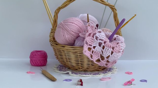 Video of process of hand crochet lace square pink doily made of cotton and acrylic yarn. Wicker basket with tools, threads, crochet hooks and knitting needles on white table