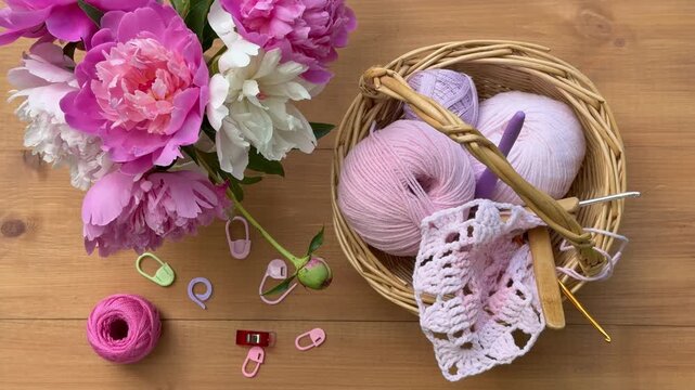 Video of summer needlework. Process of hand crochet lace square doily made of cotton and acrylic yarn. Vase with fresh pink peonies and basket with threads and hooks on wooden table