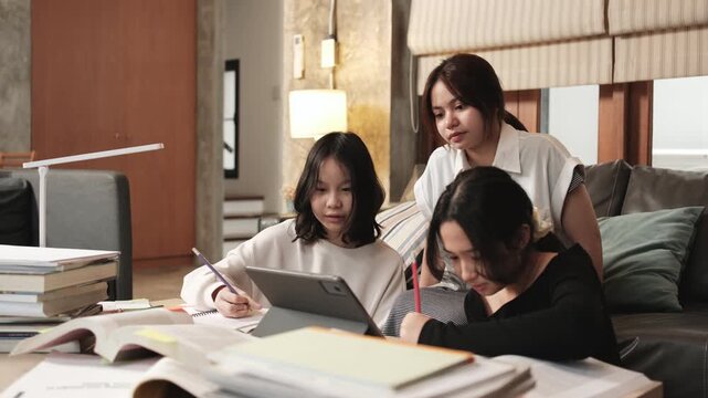 Three Asian teenage girls concentrate on online class, remote learning at home using tablet, writing and reading textbooks, self-study for back-to-school, Homeschooling education homework lifestyle.