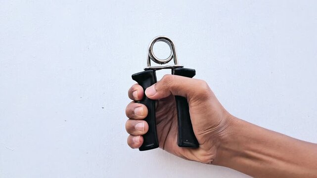 Close-up of a hand squeezing a black hand gripper for grip strength training and forearm workout on  white background.
