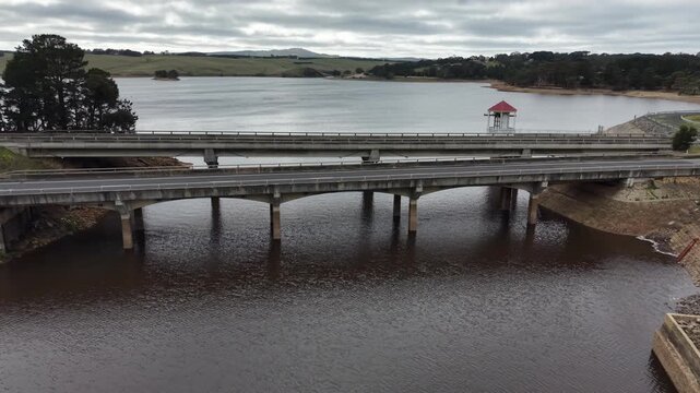 Aerial view of a car driving over a concrete bridge spanning a reservoir