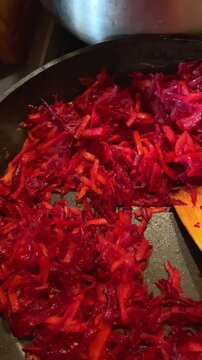 Shredded beets and carrots cooking in a hot pan stirred by a wooden spatula for a healthy meal preparation.