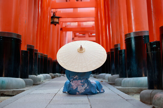 Woman in Blue Kimono Sitting on Ground with Paper Umbrella Inside Red Torii Tunnel at Fushimi Inari