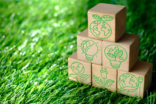 Wooden blocks stacked in a pyramid on green grass featuring green eco-friendly icons. Concept of environmental conservation, sustainable renewable energy, ESG, green business,ecology with copy space.