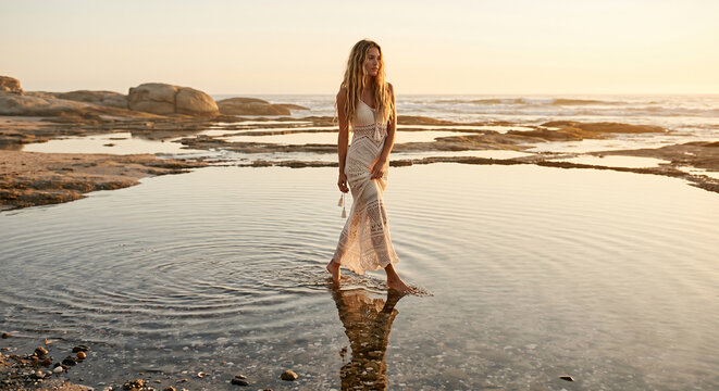 Woman in white dress walking through tide at sunset