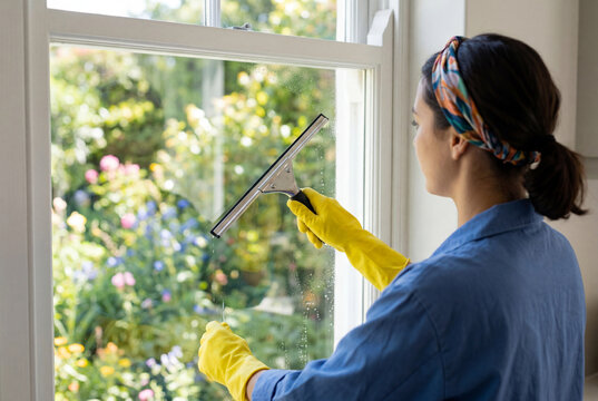 Young woman wearing yellow gloves using squeegee to clean window