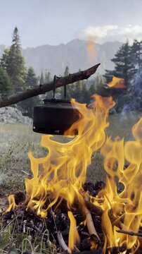Campfire on a canyon rock with traditional teapots and water background, vertical