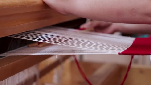 Close-up of a girl weaving red fabric on a traditional wooden handloom, preserving authentic Albanian textile craftsmanship and cultural heritage.