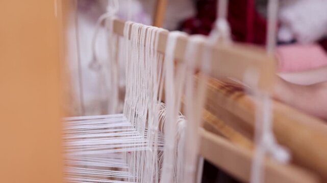 Close-up of warp threads stretched across a traditional wooden handloom as a child learns Albanian weaving techniques in a local textile workshop.