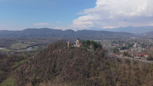 Elevated drone footage revealing Martvili Monastery perched on a hilltop, surrounded by trees and embraced by the beautiful natural landscape of western Georgia.