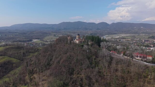 Panoramic drone shot of Martvili Monastery perched atop a hill, revealing the lush river valley and breathtaking Georgian landscape stretching into the distance.