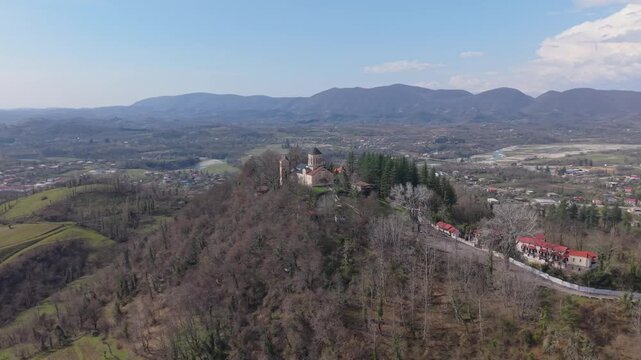 Drone orbit around Martvili Monastery perched on a hilltop, revealing the breathtaking landscape of western Georgia with lush forests and rolling countryside.