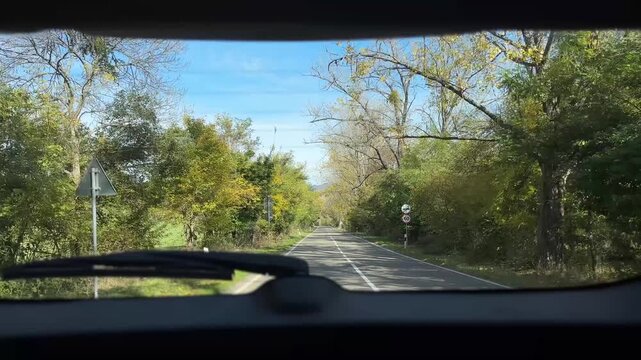 Car travels along a peaceful country road surrounded by trees showcasing stunning autumn colors. Natural beauty concept.