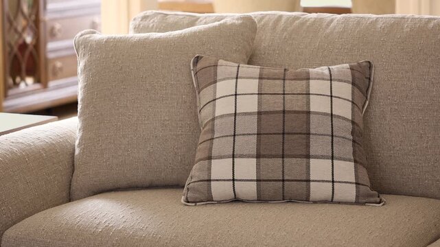 Slow zoom out of a patterned decorative cushion on a grey sofa as warm sunlight illuminates a rustic living room interior.