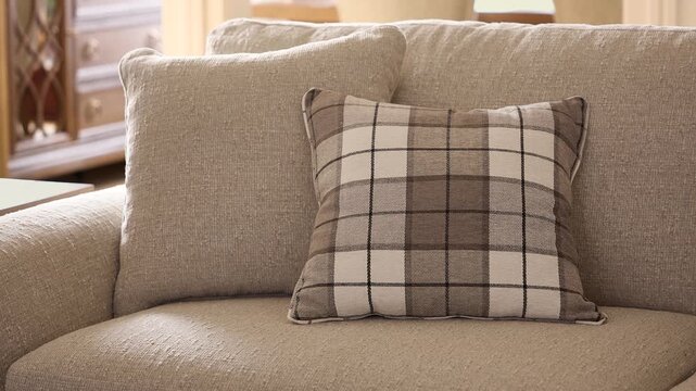 Slow zoom in on a patterned decorative cushion resting on a grey sofa with warm sunlight enhancing a rustic living room setting.