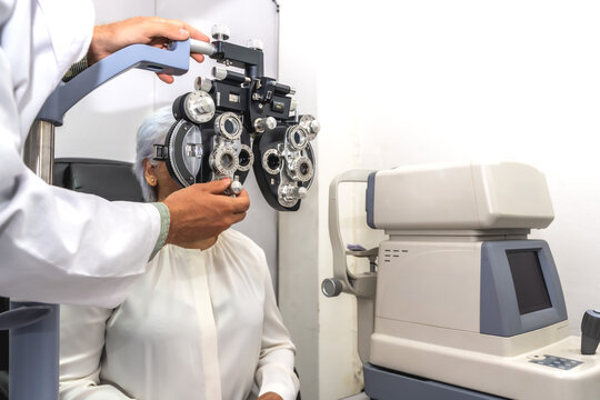Male ophthalmologist or eye doctor testing vision with modern phoropter equipment for senior female patient in eye clinic
