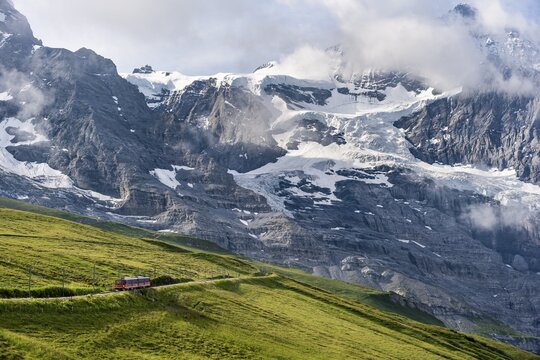 Jungfrau Railway to Jungfraujoch runs through green meadows, above the Kleine Scheidegg stop, rack railway, mountains with M&ouml;nch summit in the back, Jungfrau region, Bernese Oberland, Switzerland