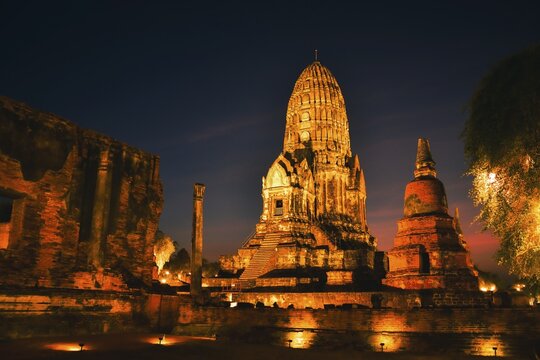 Wat Ratchaburana ancient temple in Ayutthaya Historical Park, Thailand .Towering central prang and crumbling brick ruins illuminated by warm golden lights against dark night blue hour sky