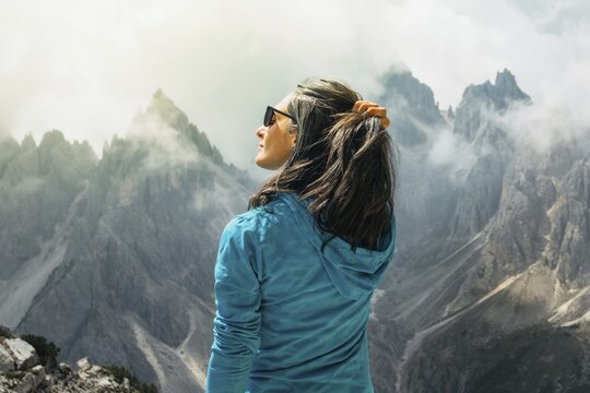 Close up profile woman hiker in turquoise fleece holding hair looking at dramatic mist covered mountain peaks background Cadini di Misurina Dolomites Italy summer
