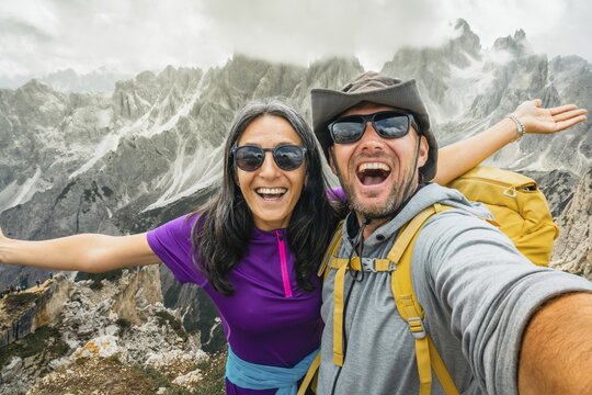 Cheerful happy couple of hikers friends taking selfie on Cadini di Misurina viewpoint. Millennial guy girl enjoying summertime day out trip laughing at camera together - Millennial travelers