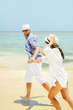 Cheerful young man leading woman couple holding hands run to beach have fun together on shallow turquoise ocean water sandy beach tropical island resort destination. Relationship honeymoon vacation