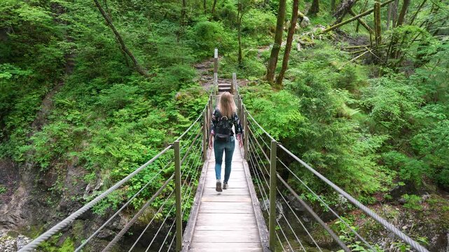 A Woman With A Backpack Crosses The Wooden Hanging Bridge In Tolmin Gorge (Tolminska Korita), Slovenia. Wide Shot