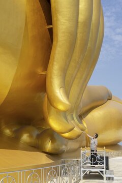 Largest Buddha statue in Thailand (Luang Pho Yai), woman 60-70 touches the fingertips of the statue because according to local belief this brings good luck and success, Wat Muang, Ang Thong, Amphoe Wiset Chai Chan province, Thailand