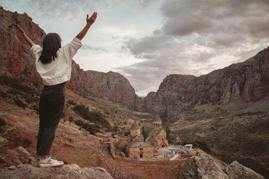 Excited happy tourist woman with outstretched arms admires the view of the famous Armenian monastery of Noravank. Travel and tourism concept